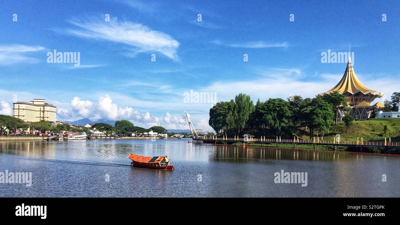 Un sampan malais traditionnel est utilisé pour transporter des personnes à travers la rivière Sarawak du bord de l'enceinte parlementaire sur la rive sud, avec l'Édifice de l'Assemblée législative de l'État, Kuching, Sarawak, Malaisie - Image de stock capturée avec un smartphone