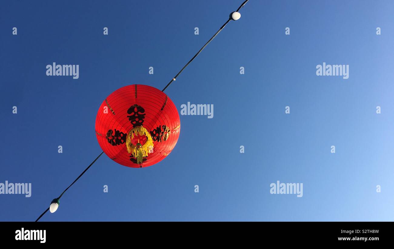 Jusqu'à la rouge vif à lanterne chinoise sur le fil avec les ampoules produits contre le ciel bleu Banque D'Images