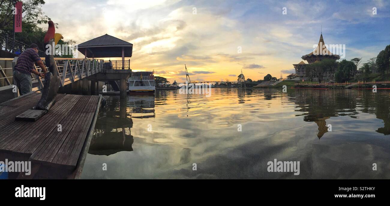 Batelier maures son Iban traditionnels malais longboat, avec un oiseau calao stylisé comme figure de proue, au bord de l'enceinte parlementaire après une croisière au coucher du soleil sur la rivière Sarawak, Kuching, Sarawak, Malaisie - Image de stock capturée avec un smartphone