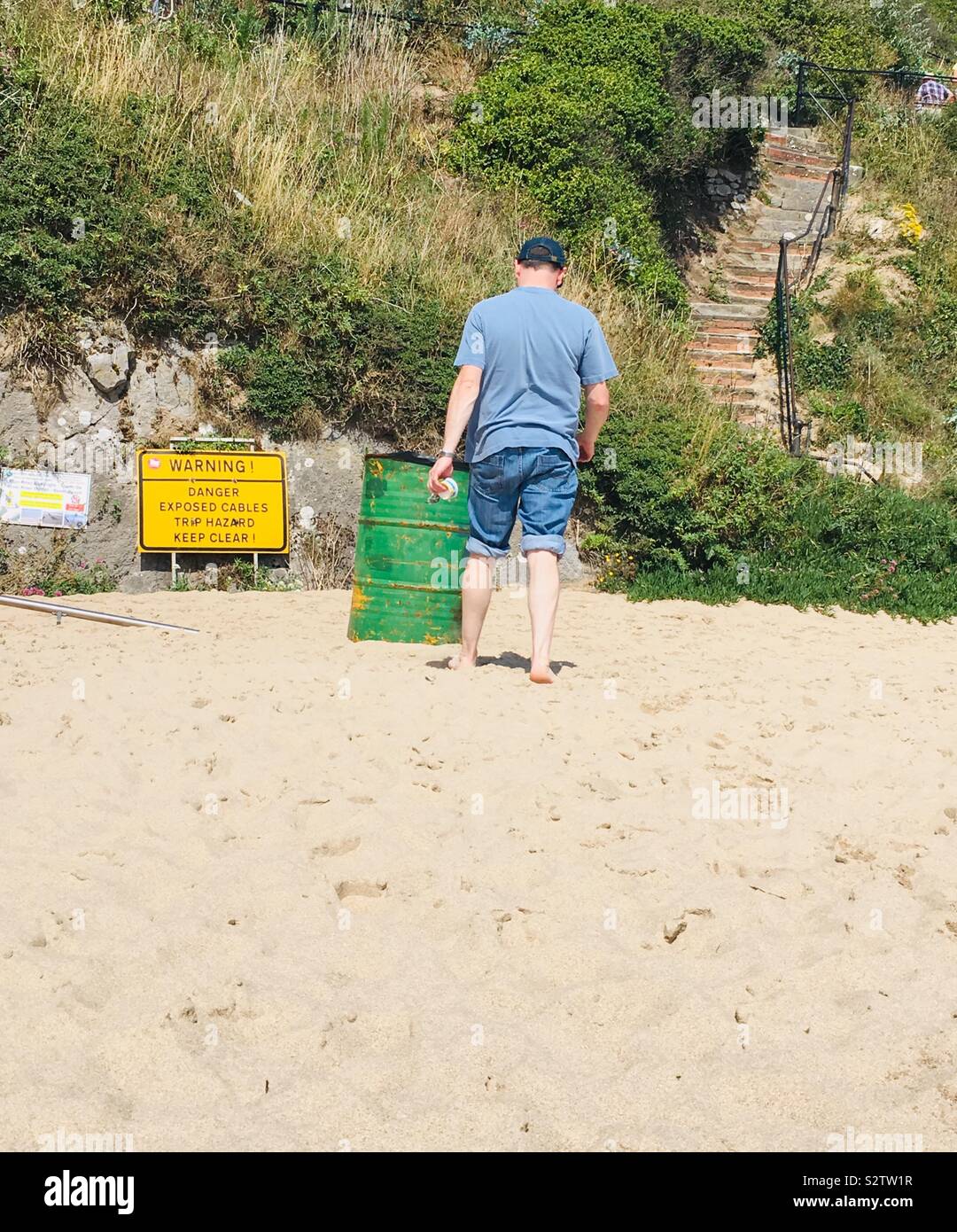 Homme portant un jean retroussé, marchant vers un bac et mise en garde sur une plage de sable fin avec accès étapes Banque D'Images