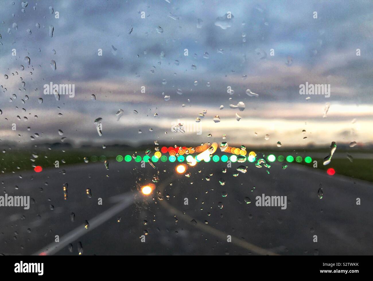 Gouttes de pluie sur la fenêtre d'un avion de ligne avec les feux de piste à l'arrière-plan comme il se prépare à décoller Banque D'Images