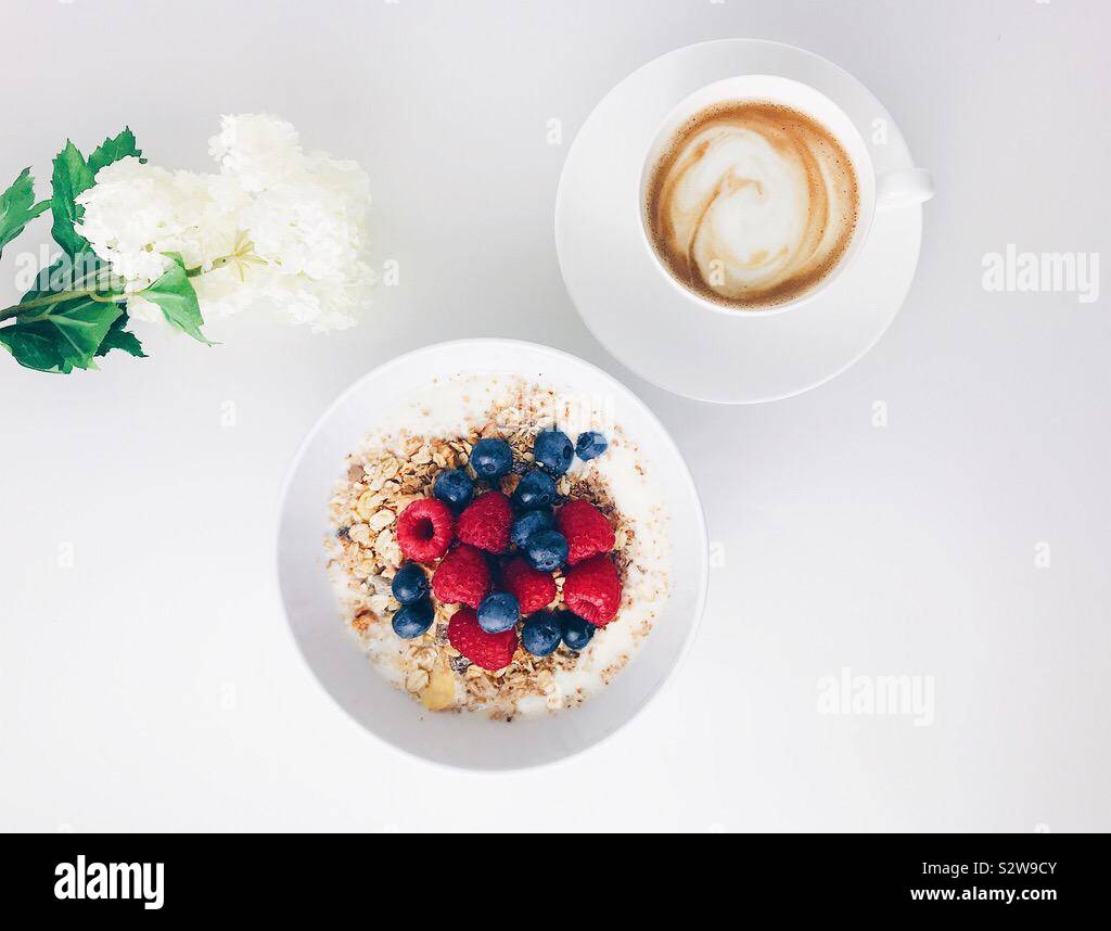 Flatlay photo de petit-déjeuner sain avec du muesli, bleuets, framboises et Café avec décoration de fleurs blanches Banque D'Images