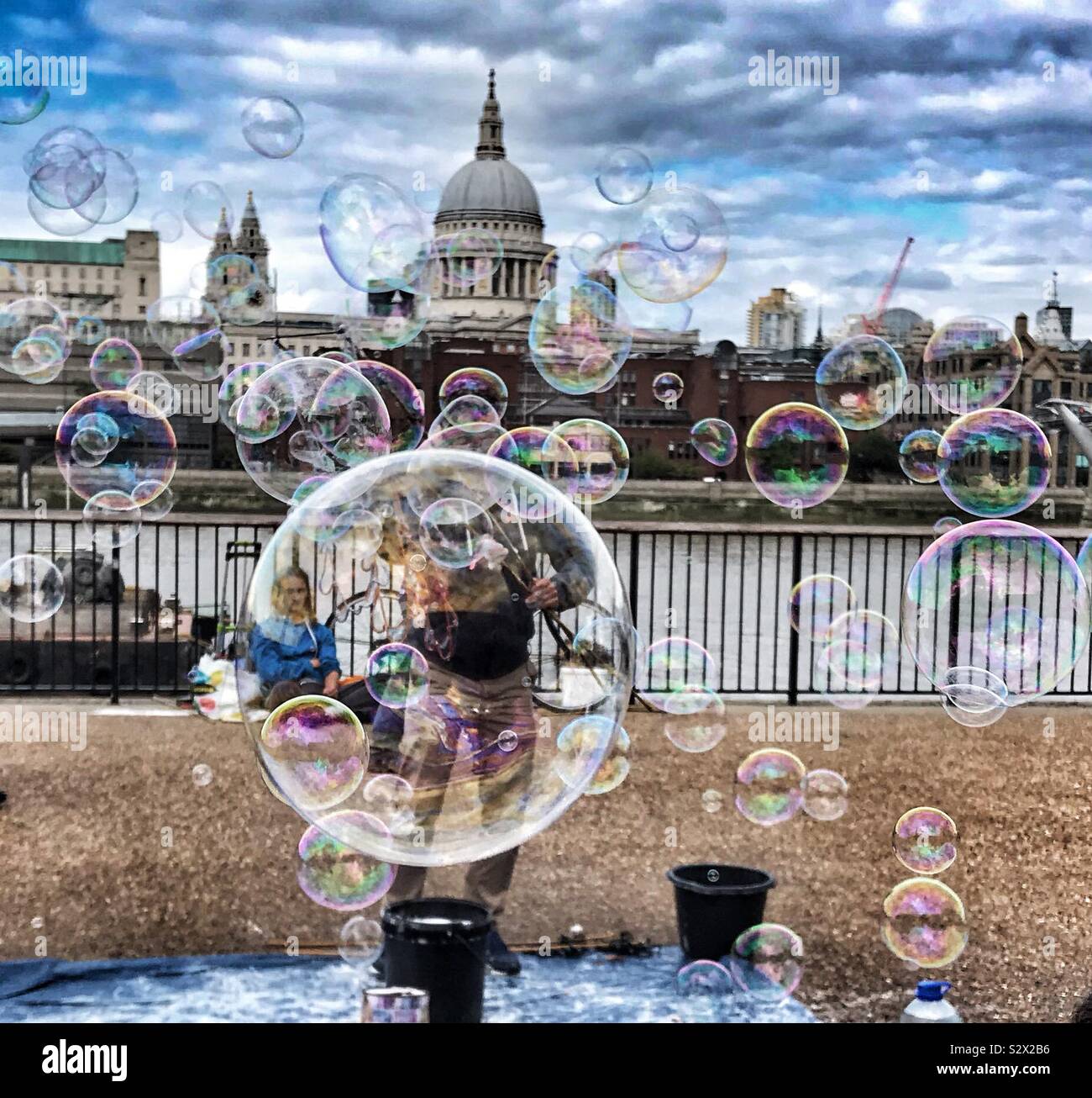 Vendeur de rue / musicien ambulant faisant des bulles le long de la Tamise avec St.Pauls cathédrale en arrière-plan - London UK Banque D'Images