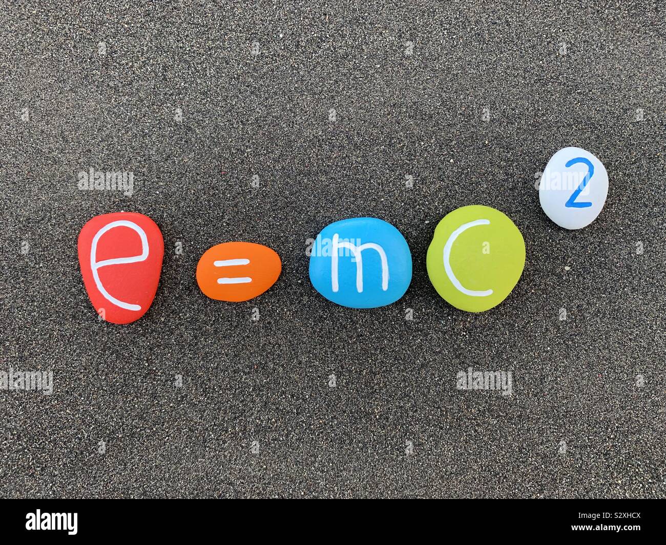 E =mc2 Théorie de la relativité composé avec des pierres colorées et sculptées sur sable volcanique noir Banque D'Images
