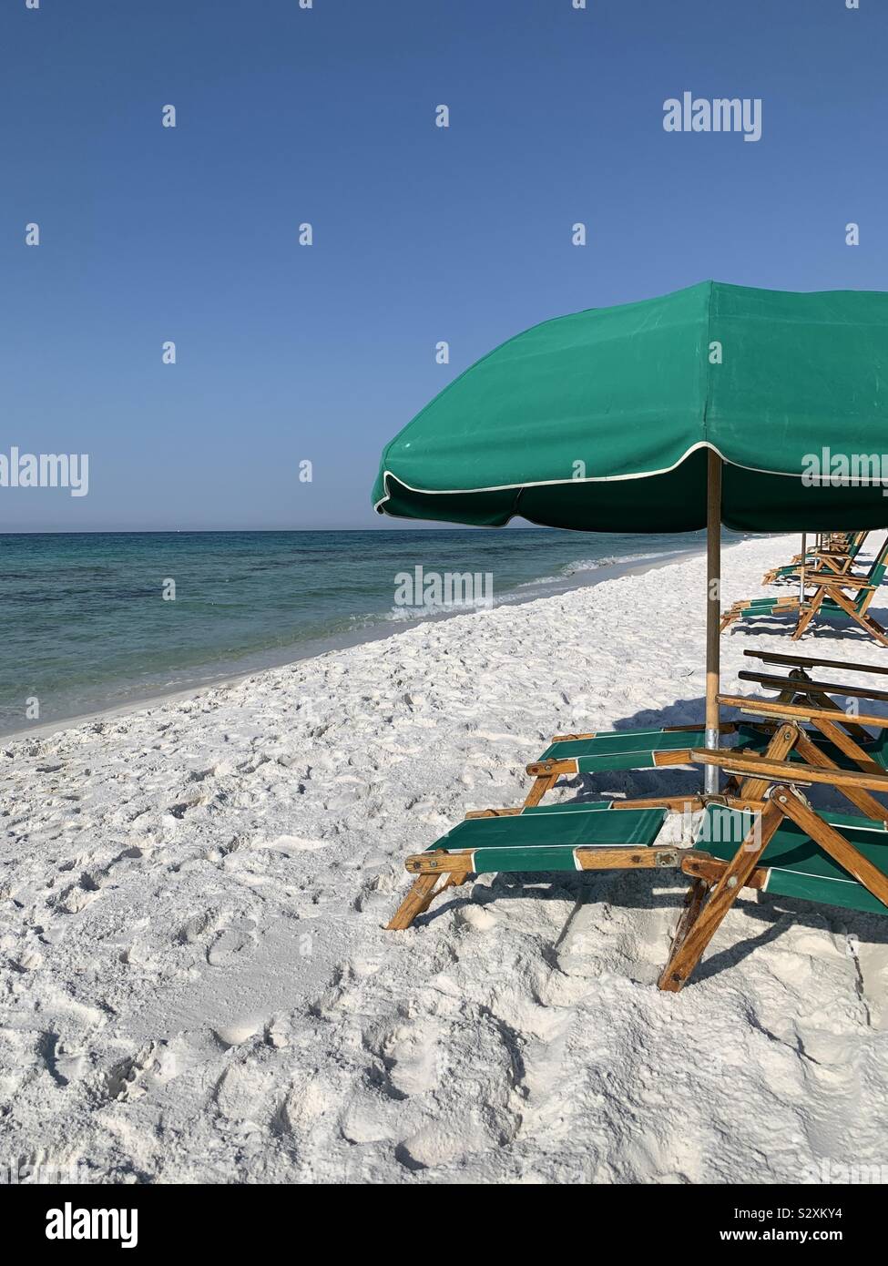 Vert couleur des chaises longues et des parasols sur la plage de sable blanc avec vue sur les eaux bleu turquoise et ciel bleu Banque D'Images