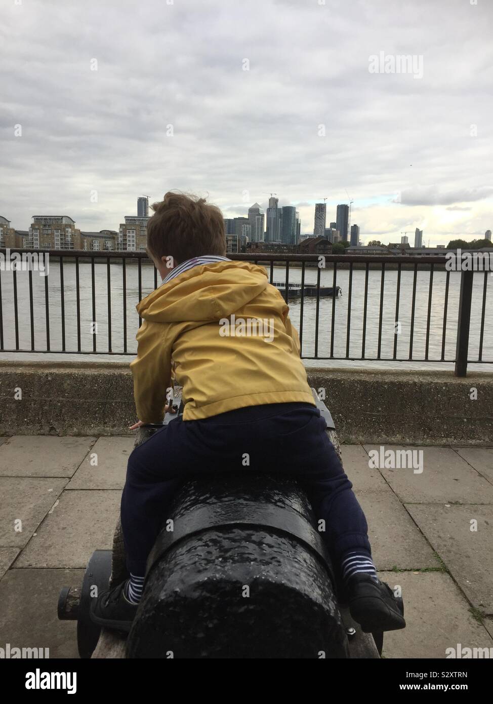 Enfant assis sur plus de canon naval de Londres Greenwich Thames manteau jaune - Image de stock capturée avec un smartphone