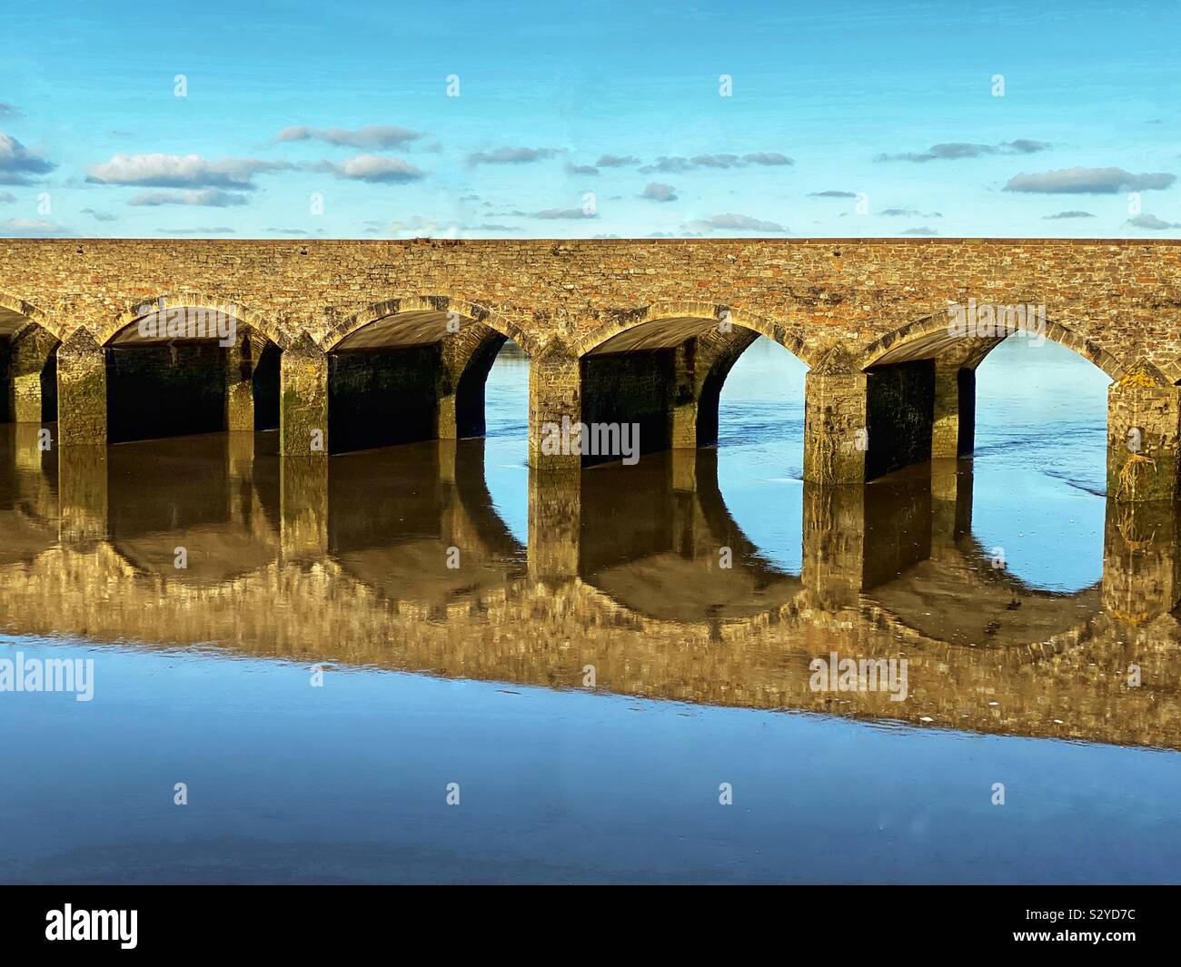 Pont en arc tôt le matin, la lumière reflétée dans l'eau encore Banque D'Images