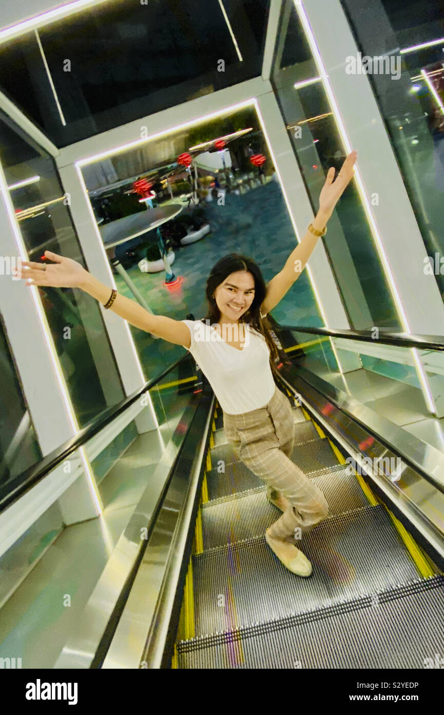 Asian girl arms wide sur esculator dans cadre blanc, de plaisir. Banque D'Images