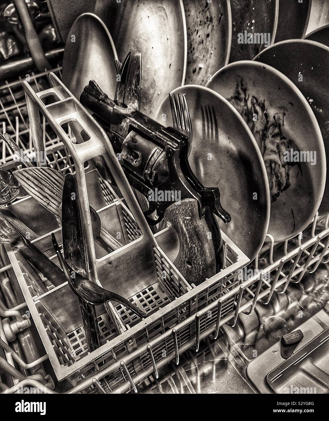 Image en noir et blanc de pistolet en lave-vaisselle entre les assiettes et couverts Banque D'Images