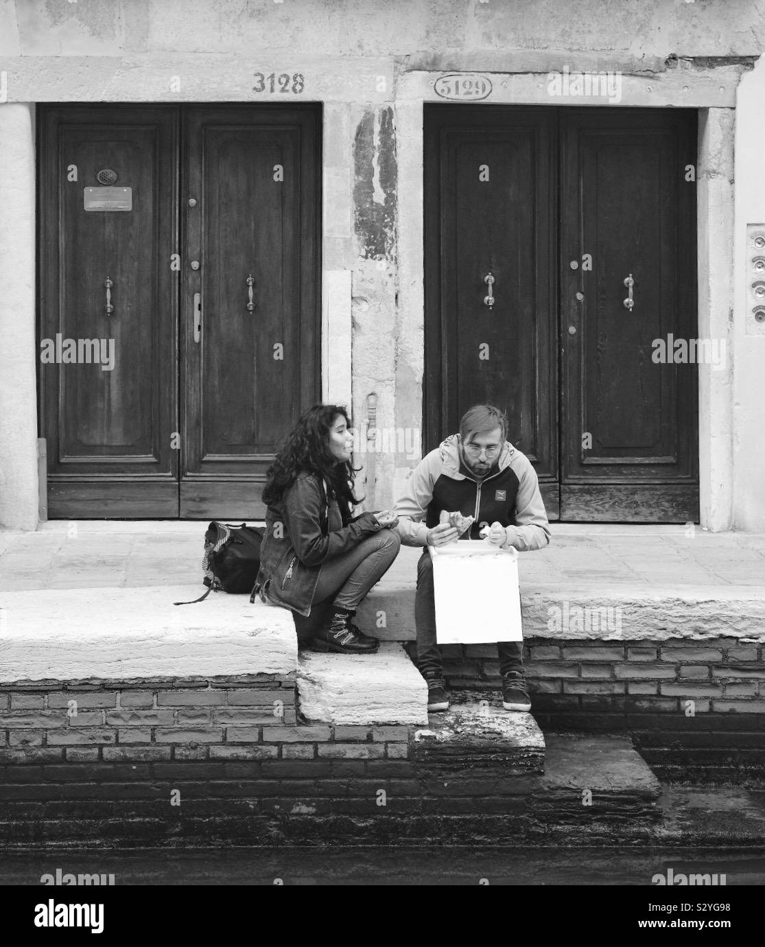 Un couple de manger le déjeuner et bavarder assis par un canal à Venise Italie Banque D'Images