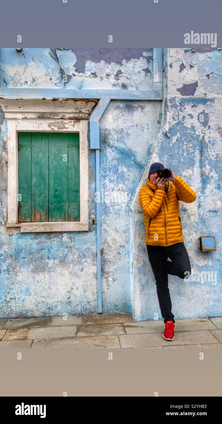 Photographe appuyé contre un mur coloré en Burano Italie avec une fenêtre aux volets verts - Image de stock capturée avec un smartphone
