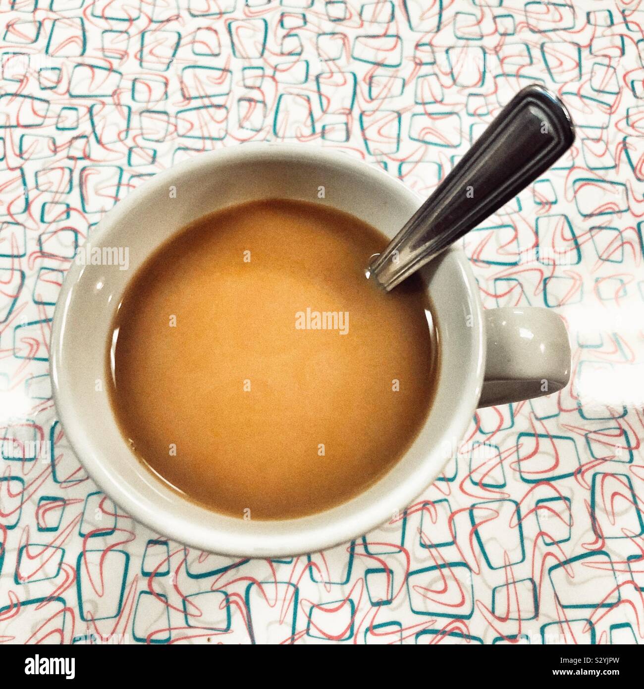 Vue rapprochée du dessus de café en blanc mug avec cuillère en argent sur table à motifs rétro - Image de stock capturée avec un smartphone