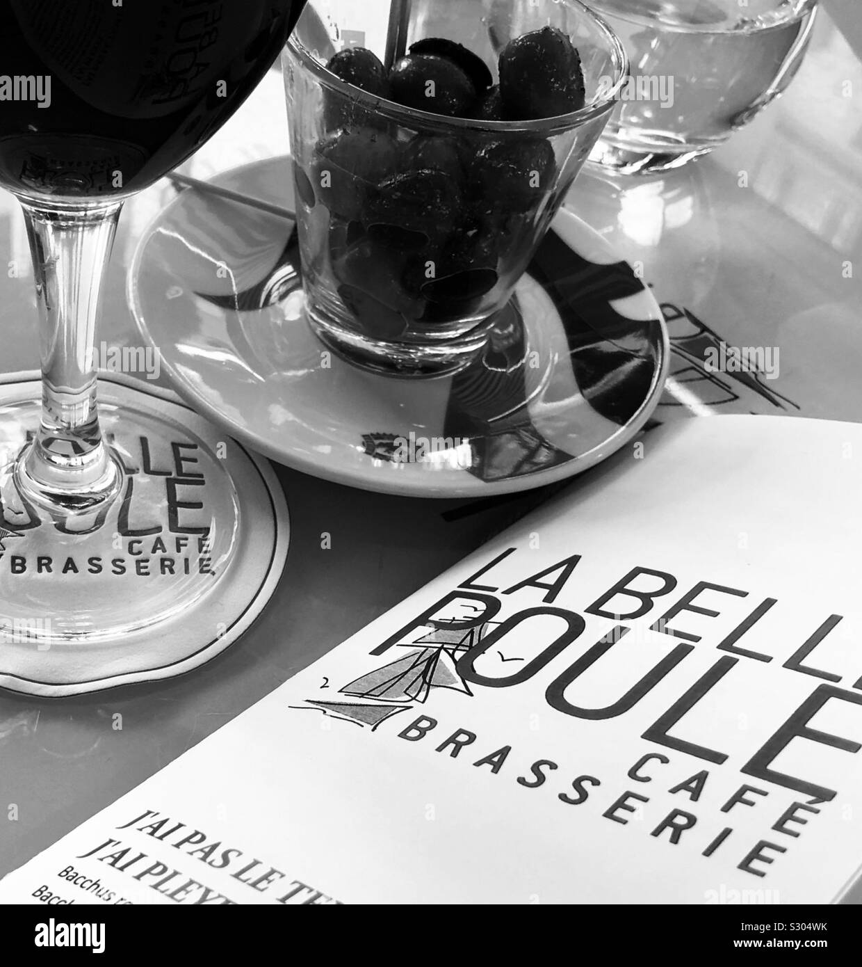 Olives, un verre de vin et le menu sur la table à la Brasserie La Belle Poule dans le 8ème arrondissement de Paris, France. Photo en noir et blanc. Banque D'Images