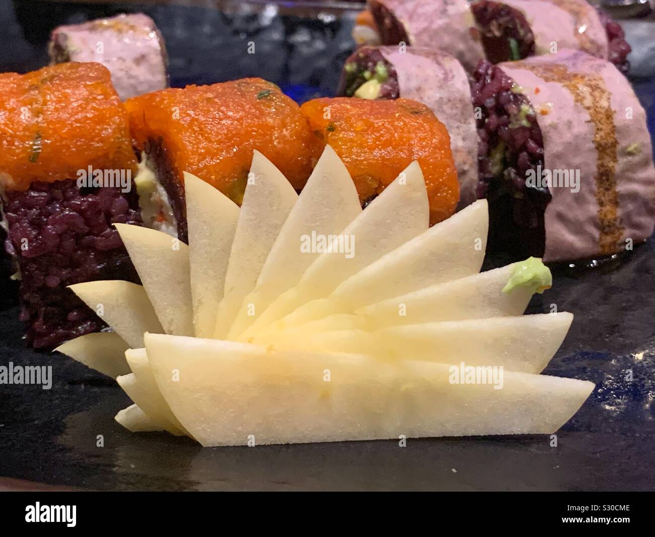 Fan de tranches de pomme de garnir une assiette de rouleaux de sushi frais - Image de stock capturée avec un smartphone