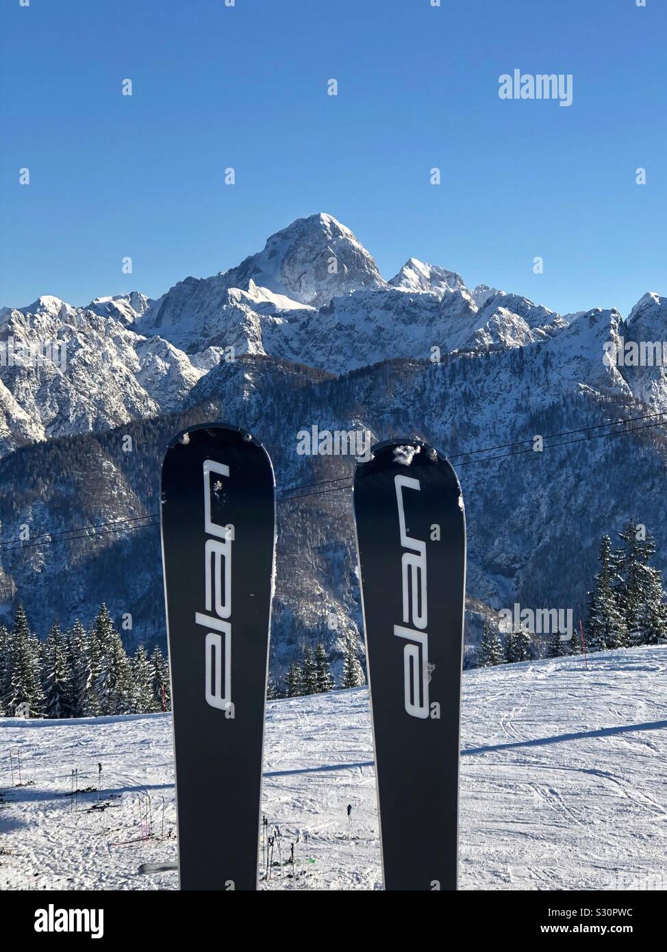 Elan skis coincé dans la neige en station de ski de Monte Lussari, Frioul-Vénétie Julienne, Italie. Alpes Juliennes en arrière-plan. Banque D'Images