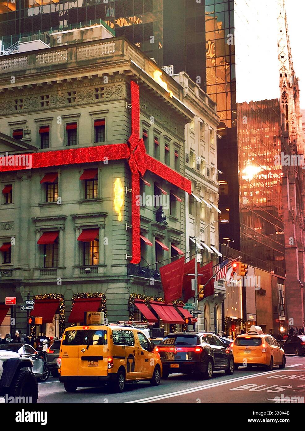 Le magasin phare de Cartier, le célèbre bijoutier est enveloppé dans un arc rouge et décoré pour les vacances pendant que le trafic se déplace sur la 5ème Avenue, New York City, États-Unis - Image de stock capturée avec un smartphone