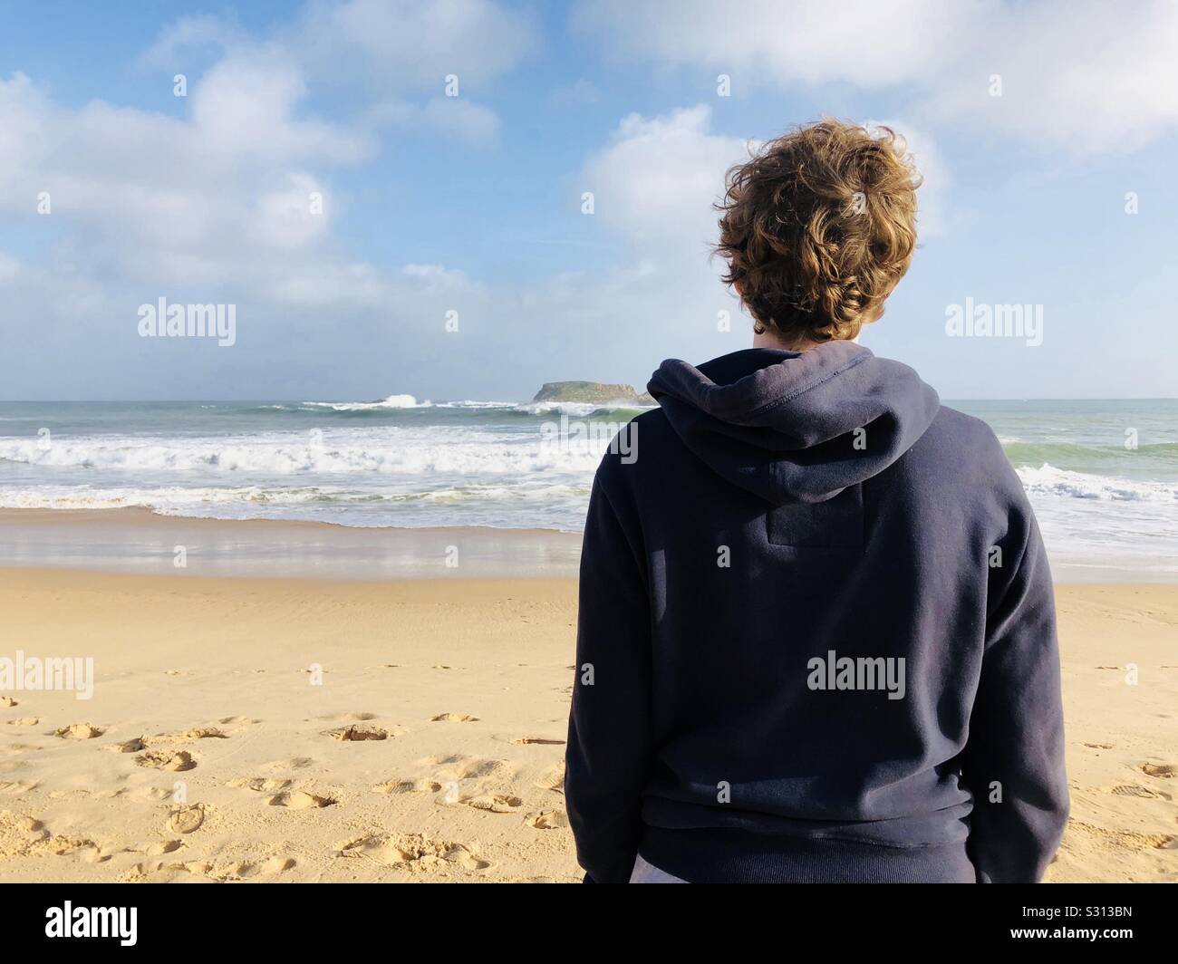 Teenage boy standing on a beach face à la mer Banque D'Images