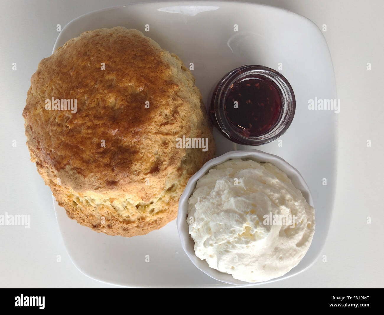 Un scone, de crème et de confiture sur une plaque carrée. Banque D'Images