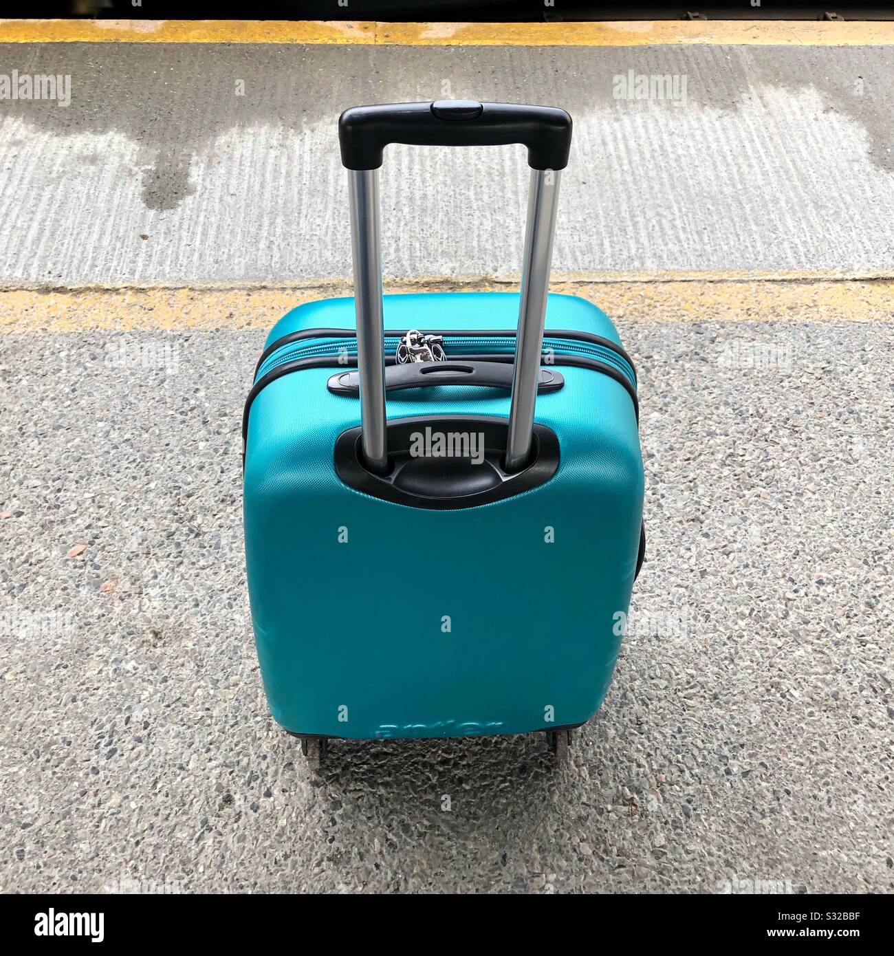 La valise turquoise avec poignée de traction étendue se tenait sur une plate-forme de gare, attendant l'arrivée du train. Banque D'Images La valise turquoise avec poignée de traction étendue se tenait sur une plate-forme de gare, attendant l'arrivée du train. Banque D'Images