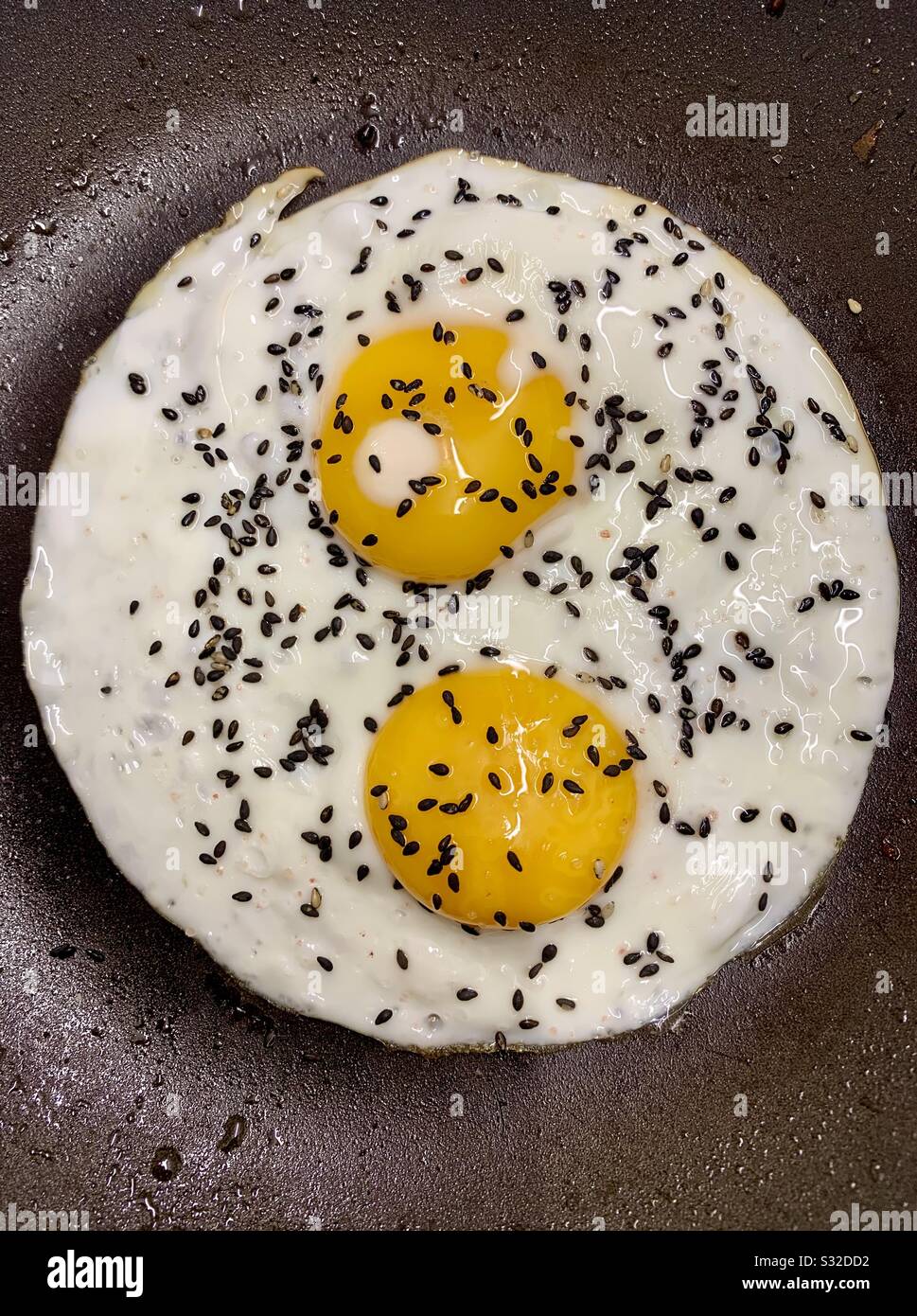 Deux œufs frits avec des graines de sésame noir dans une poêle à frire Banque D'Images