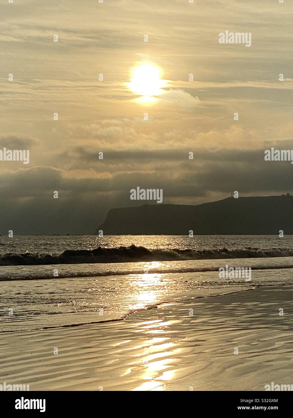 Le soleil doré se couche sur une plage dans le sud de la Californie avec des vagues basses qui roulent dans le surf. - Image de stock capturée avec un smartphone