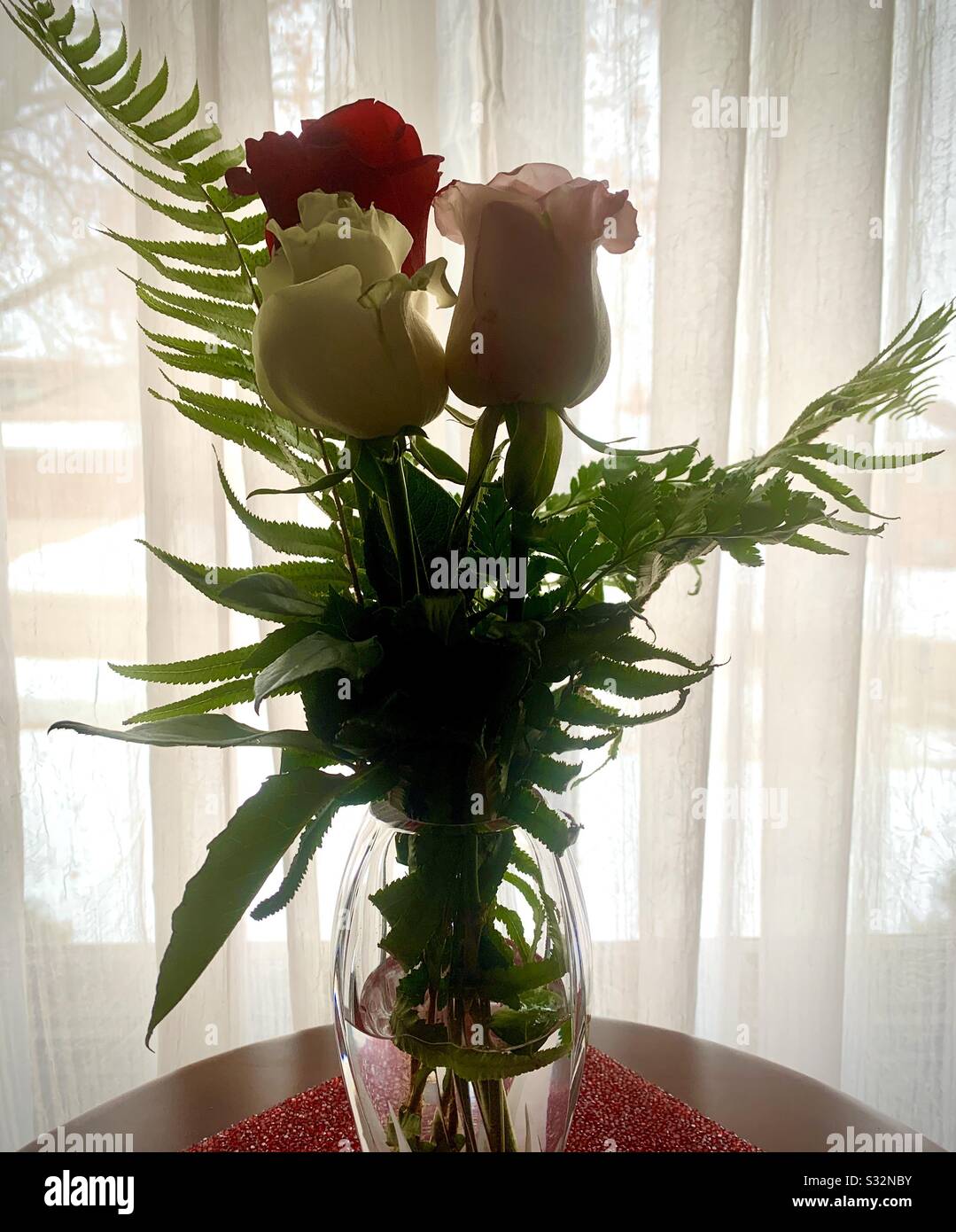 Dubuque, IOWA, 01/29/20–gros plan photo de belles roses rouges et blanches avec des fougères vertes placées dans un vase en cristal avec rose rose rose posée sur un placéme rouge brillant en premier plan. Banque D'Images