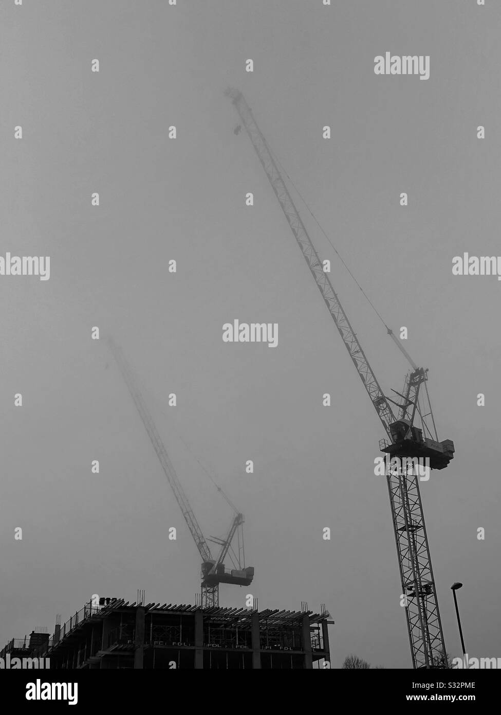 Deux grues de construction disparaissent dans le brouillard un matin sombre et sombre. Banque D'Images