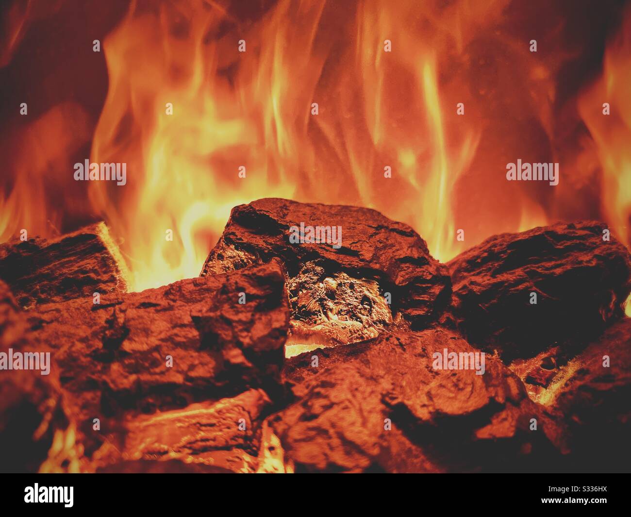 Gros plan de mise au point sélective à l'intérieur d'une cheminée. Détails des coals chauds avec des flammes à la hausse orange et jaune. Éclairage atmosphérique avec espace de copie - Image de stock capturée avec un smartphone