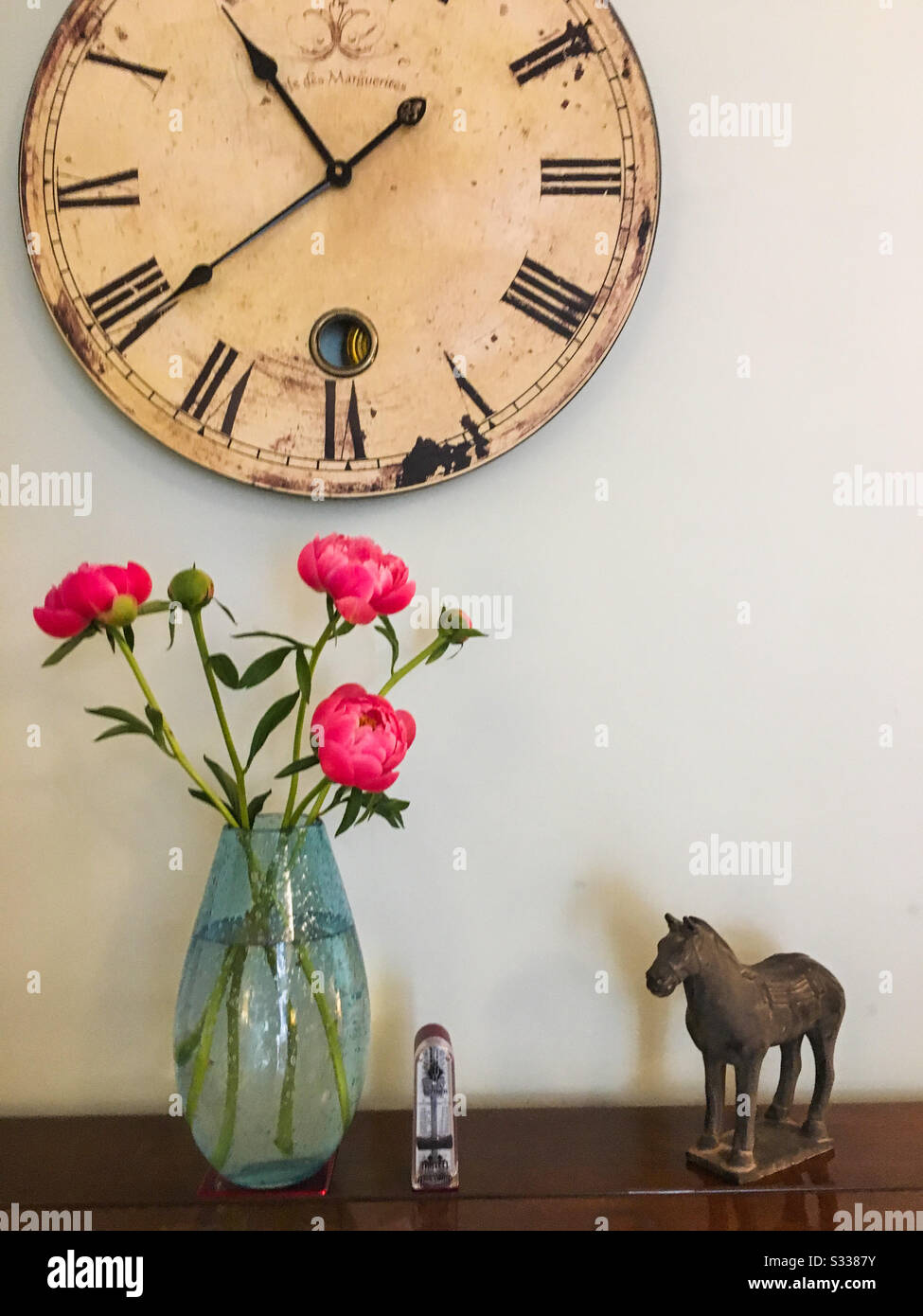 Une photo de vie fixe avec des fleurs pivoines, une horloge, un métronome et un ornement oriental de cheval. Banque D'Images