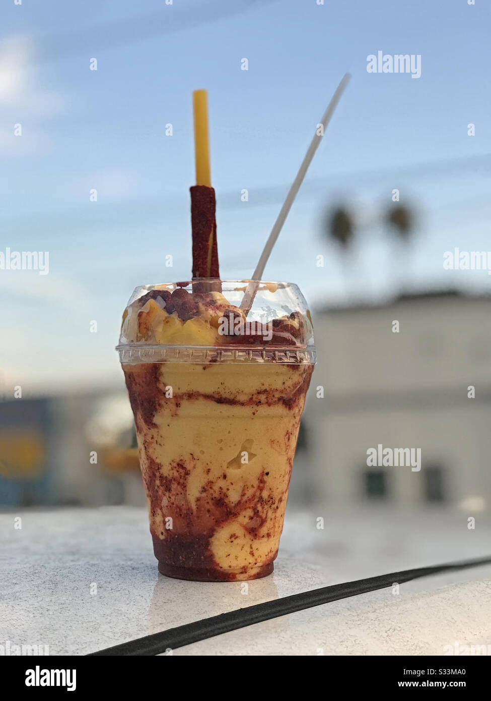 Une boisson traditionnelle gelée de mangonada mexicaine, composée de sorbet de mangue, de morceaux de mangue, de chamoy, de chaux, de poudre de tajin et de bonbons de tamarin, est présentée dans une tasse en plastique transparent. Banque D'Images
