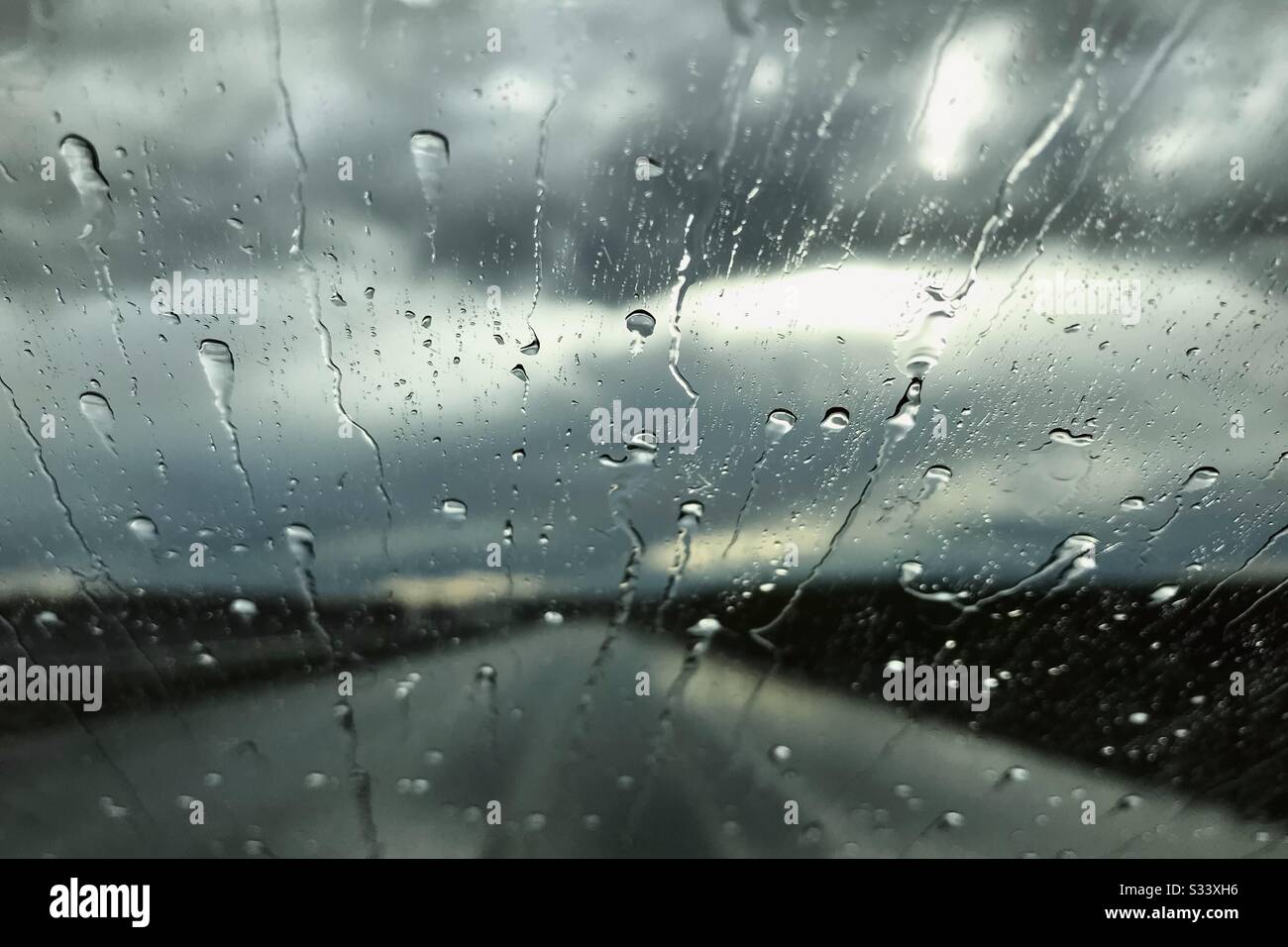 La pluie tombe sur un pare-brise de voiture. Vue sur la journée des pluies à travers une fenêtre de voiture. Concept de saison des pluies. - Image de stock capturée avec un smartphone