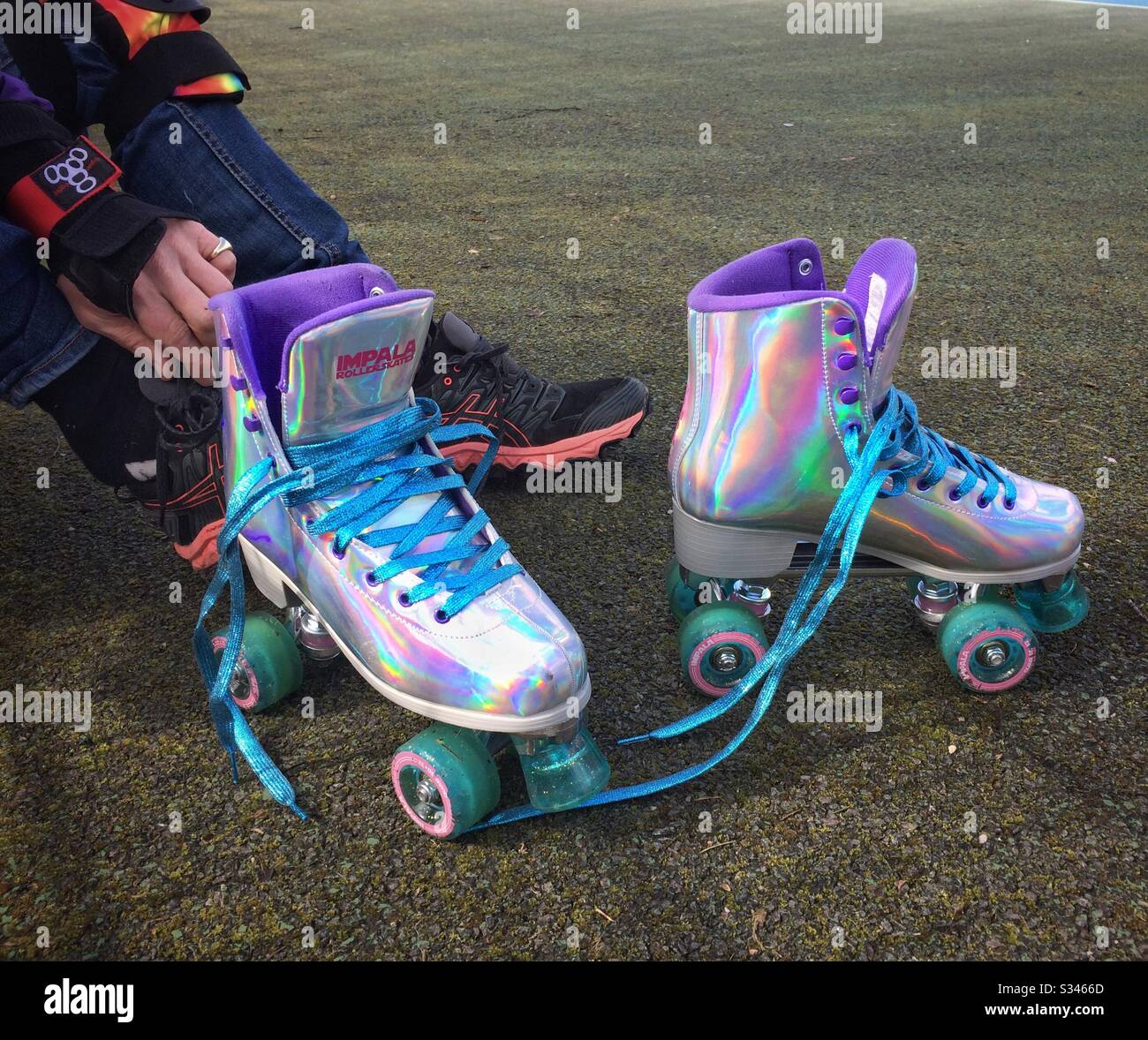 L'homme remettant ses chaussures après une séance de patinage à roulettes en plein air dans des patins à roulettes holographiques argentés Banque D'Images