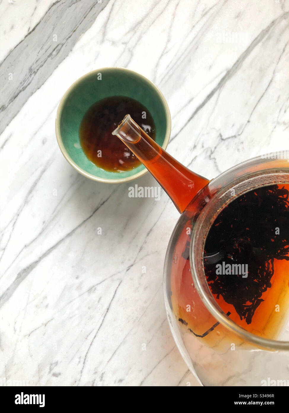 Le thé à feuilles mobiles pu-erh de Chine est versé d'une théière en verre dans une tasse en céramique verte vernie. Ce type de thé noir fermenté est sain et aide à la digestion des graisses. Banque D'Images