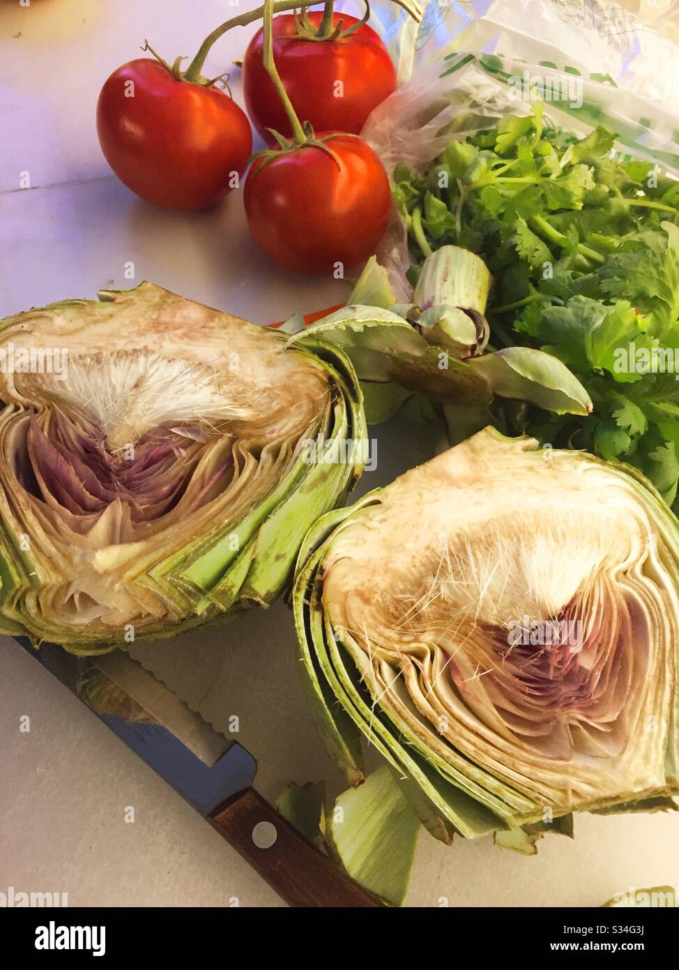 Gros plan sur un artichaut en tranches, des tomates et un bouquet de cilantro sur une planche à découper de cuisine résidentielle, États-Unis Banque D'Images