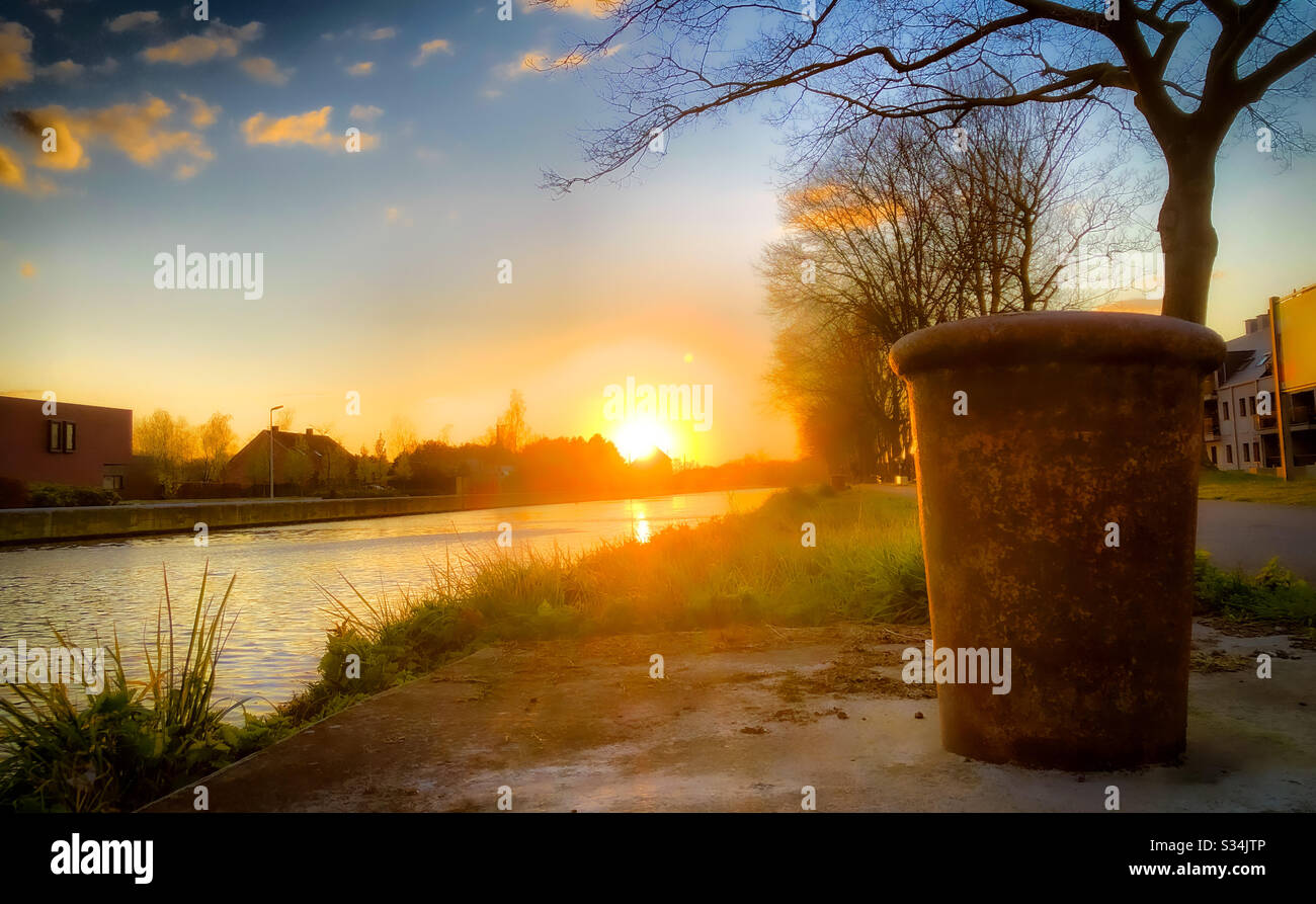 Poteau métallique rouillé sur la rive d'un canal sous un ciel doré au coucher du soleil, Kempen, Belgique - Image de stock capturée avec un smartphone