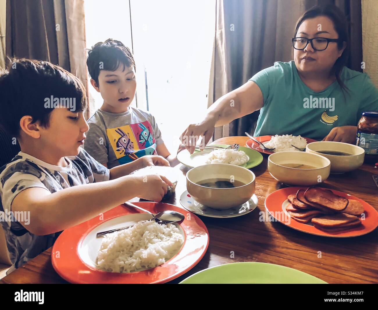Une famille mangeant un repas ensemble à une table à manger. La table est recouverte de bols et de assiettes avec du riz, de la viande et de la soupe. Banque D'Images