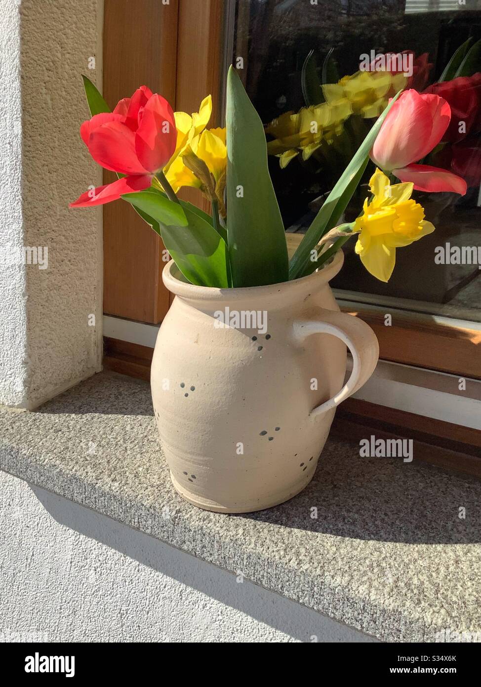 Daffodil et tulipes rouges dans le pot sur le seuil extérieur de la fenêtre Banque D'Images