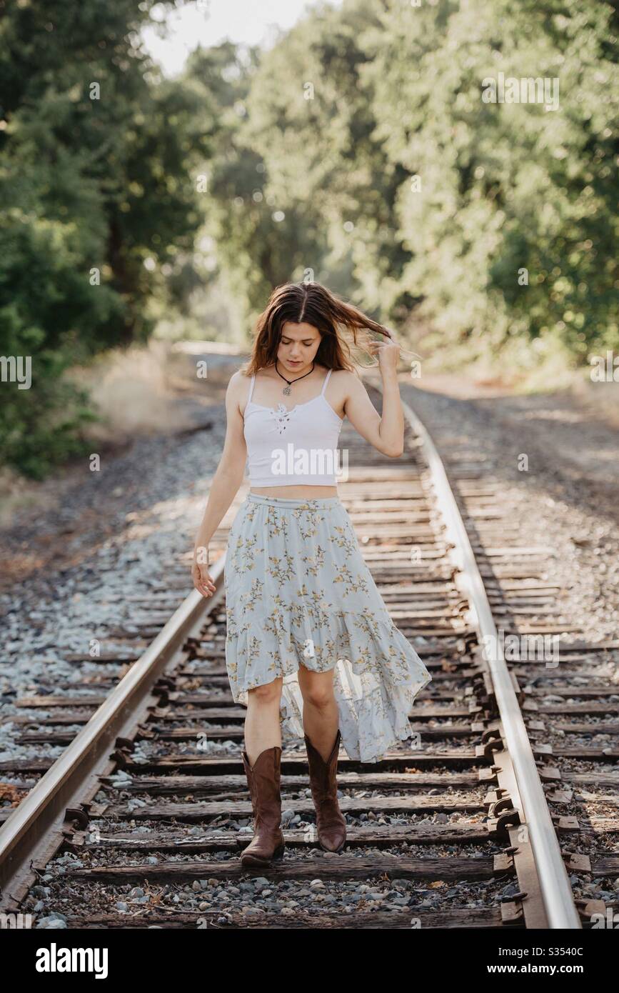 Fille dans des bottes de cowboy brunes sur les voies de train portant une  jupe verte et bleue Photo Stock - Alamy