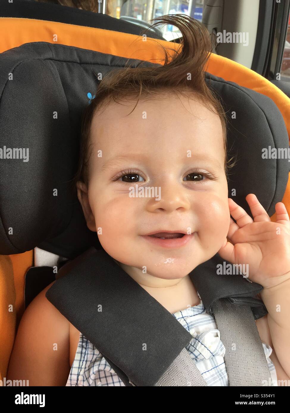 Garçon tout-petit assis dans un siège d'auto, souriant avec une boucle dans ses cheveux. - Image de stock capturée avec un smartphone