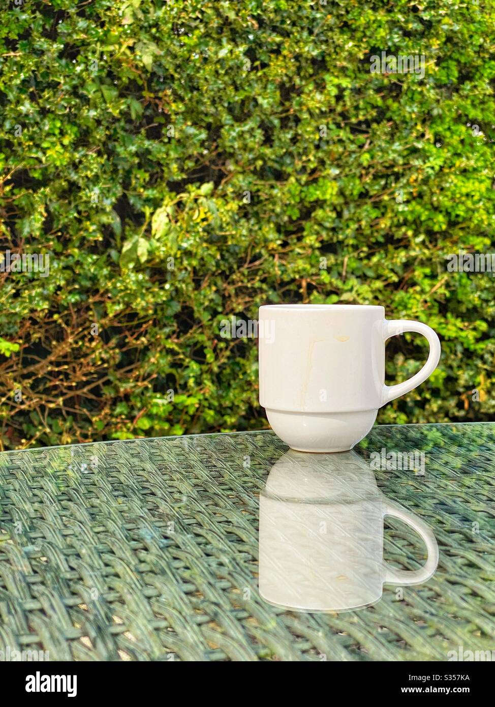Tasse à café blanche sur mobilier de jardin avec miroir dans un plateau de table en verre Banque D'Images