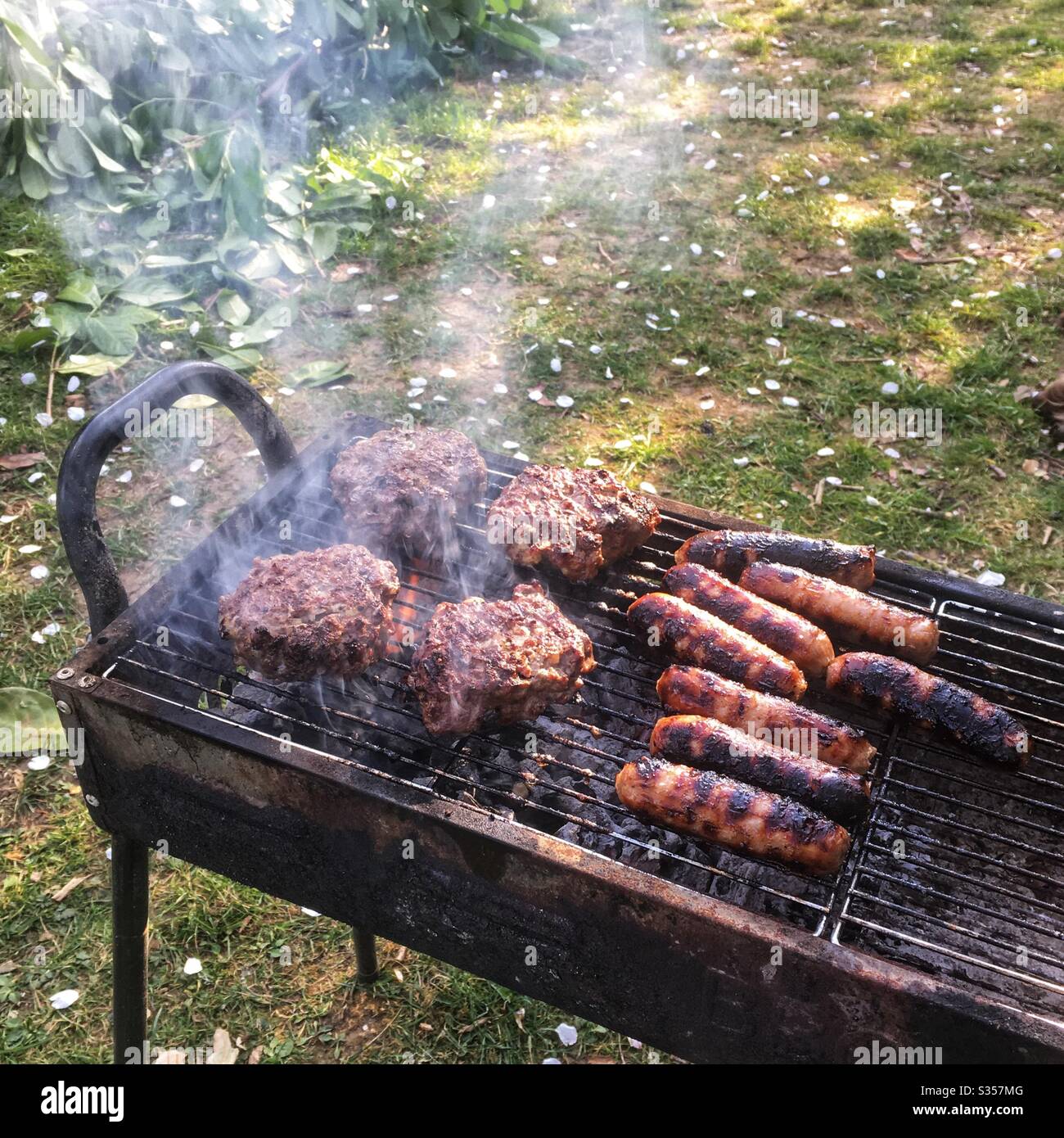 Des hamburgers de bœuf et des saucisses cuisant sur un barbecue. Hampshire, Angleterre, Royaume-Uni. - Image de stock capturée avec un smartphone