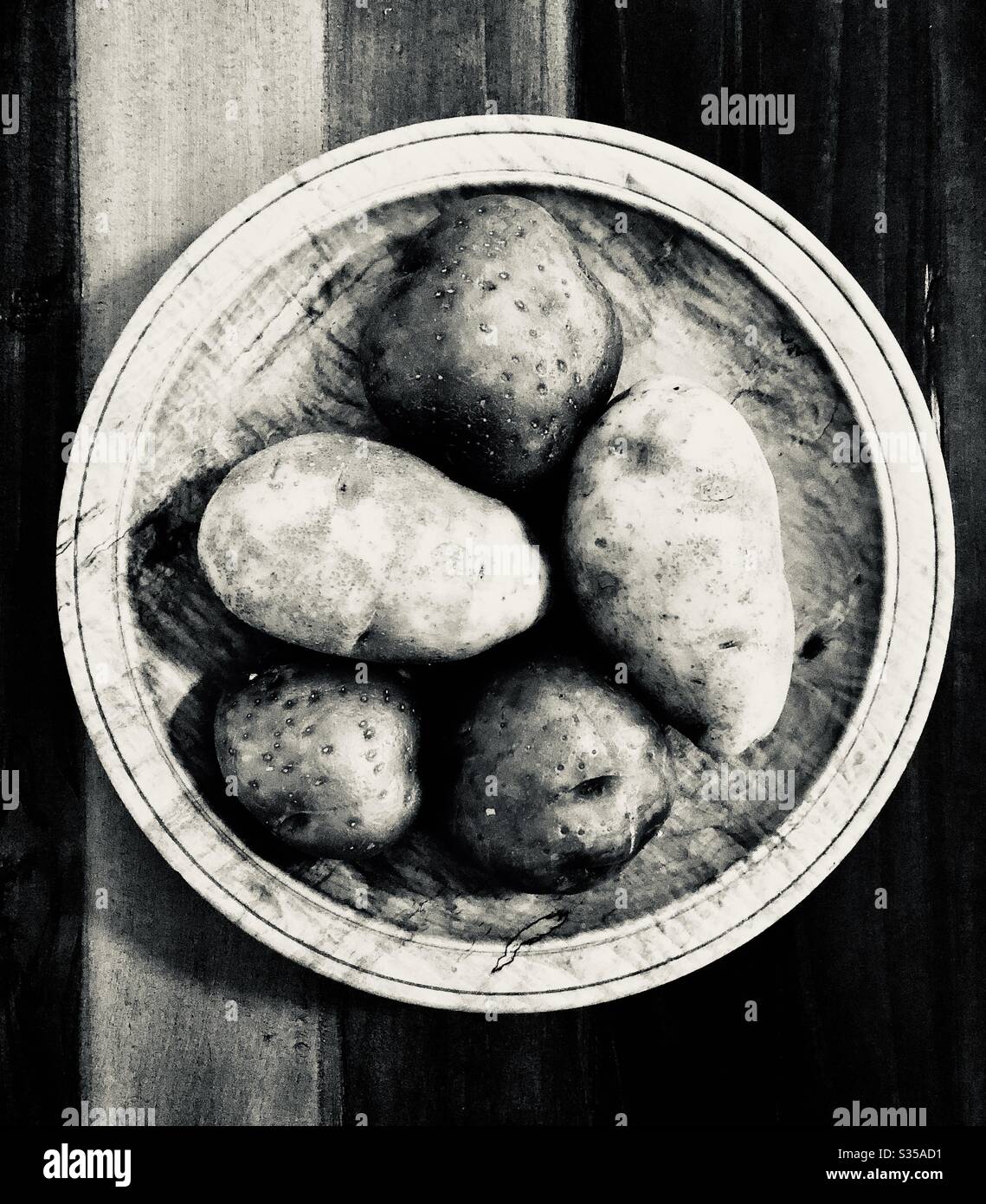 Photo monochromatique de pommes de terre de 5’ sur un bol en bois et une table. Banque D'Images