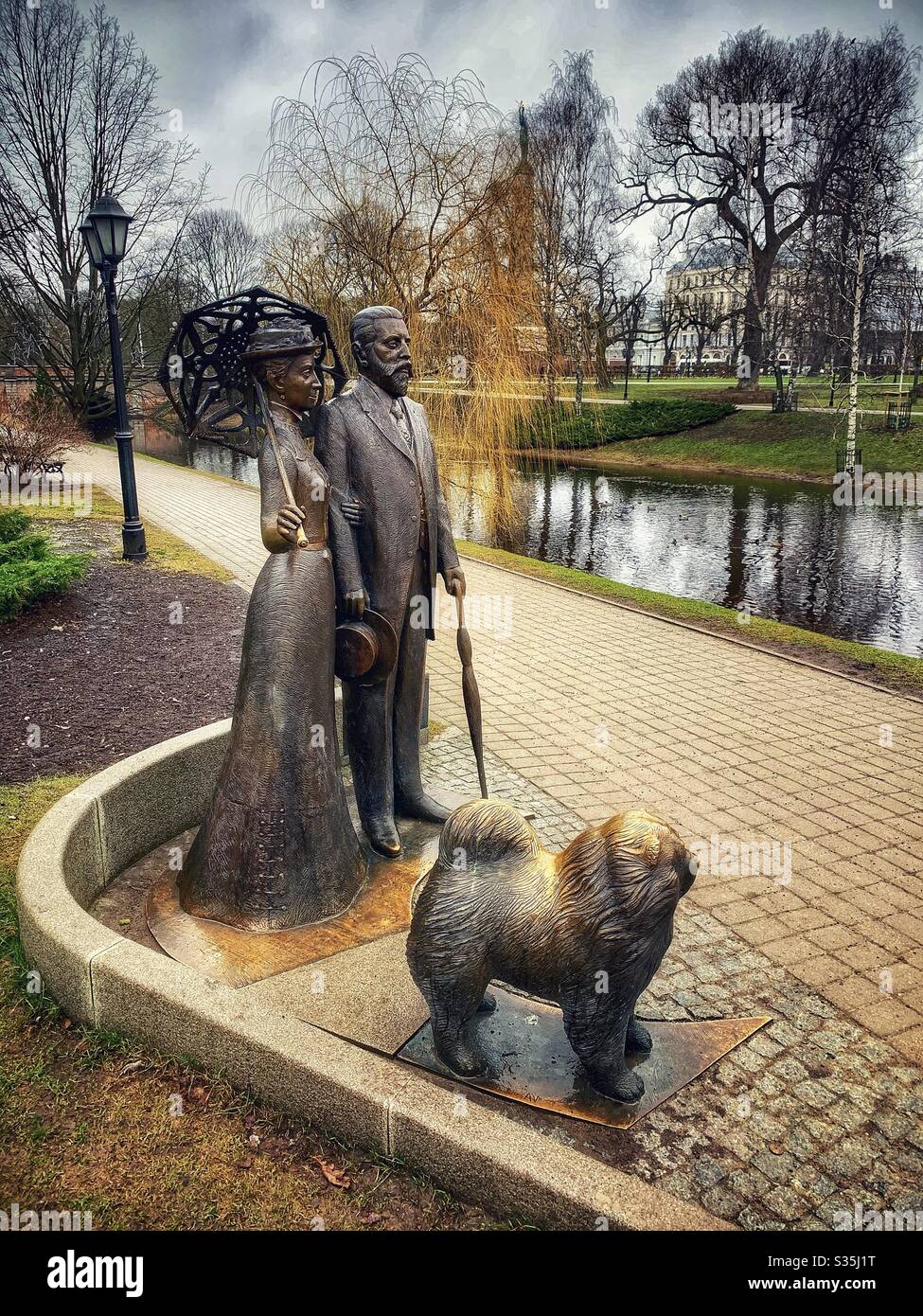 Statue en bronze d'un homme et d'une femme dans des vêtements à l'ancienne avec leur chien et leurs parasols. Dans un beau parc à Riga, Lettonie. À côté de la rivière. - Image de stock capturée avec un smartphone