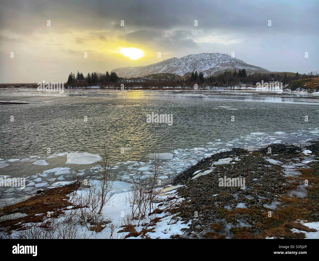 La glace coule sur une rivière en Islande, avec le soleil bas sur le point de se coucher derrière une montagne enneigée en arrière-plan. - Image de stock capturée avec un smartphone