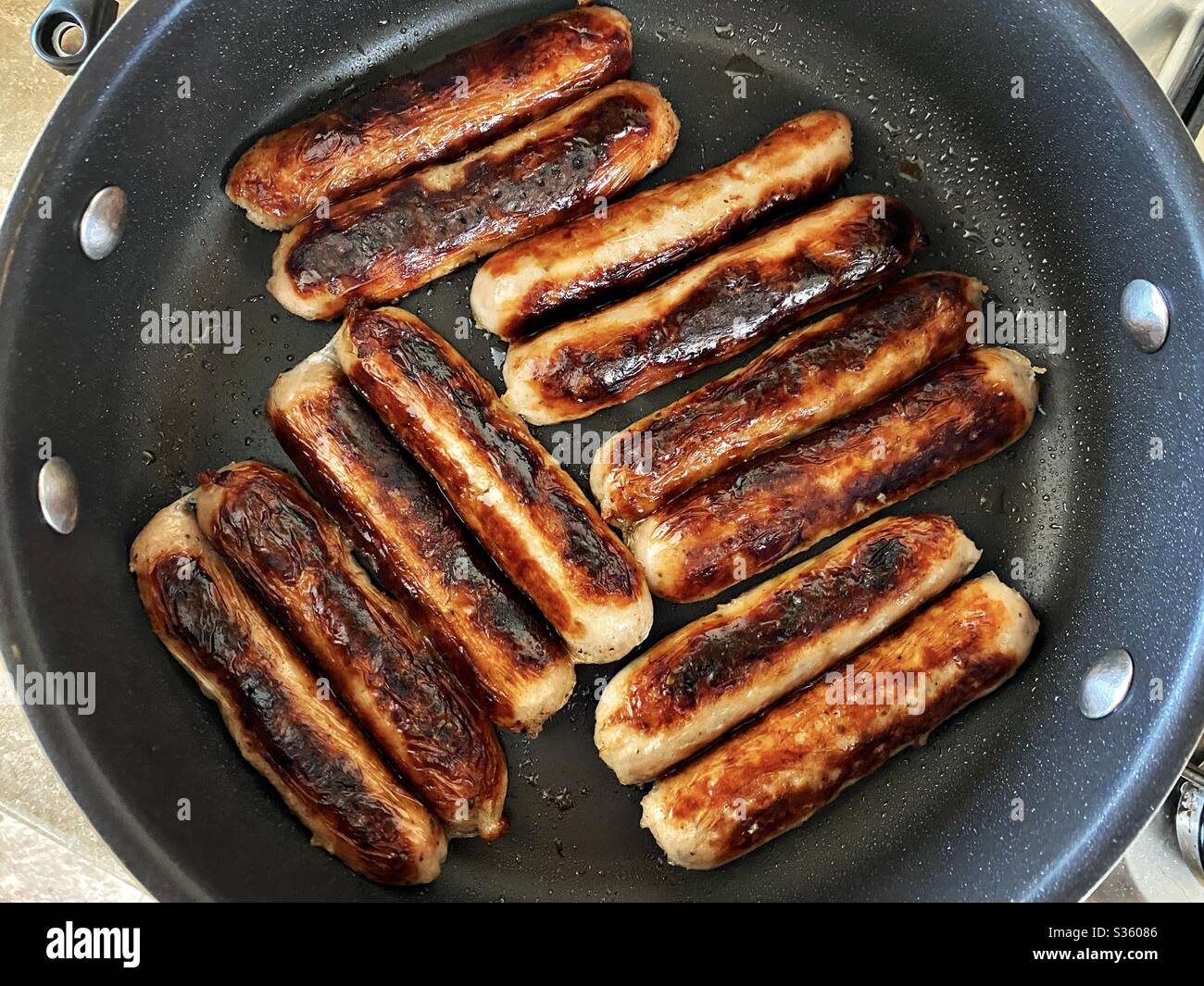 Vue rapprochée des saucisses de porc Cumberland fraîches qui se sirotent dans une poêle. Nourriture grasse et savoureuse. Petit déjeuner traditionnel anglais à base de viande dans une grande poêle à frire. Banque D'Images