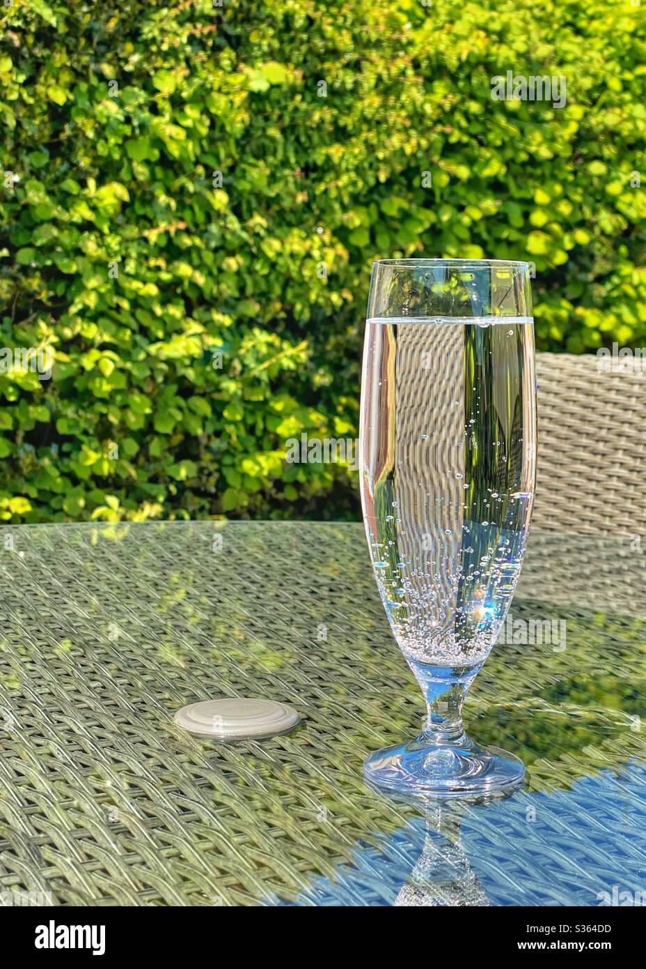 Grand verre d'eau minérale gazeuse sur la table en verre du mobilier de jardin Banque D'Images