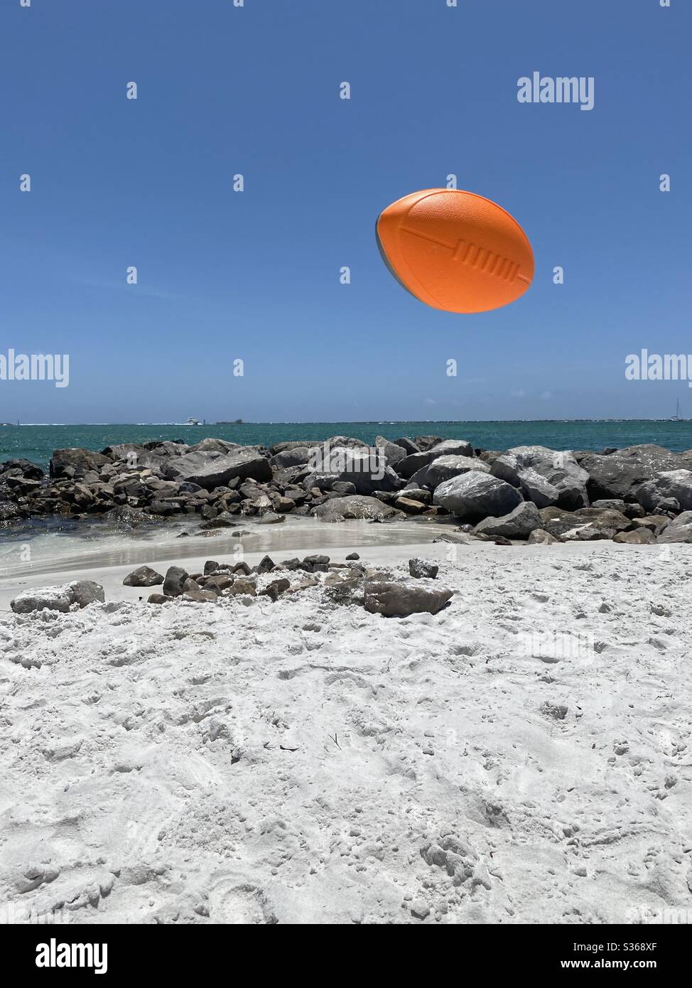 Un football en plein air sur une plage de sable blanc avec vue sur le rivage rocheux et l'eau Banque D'Images