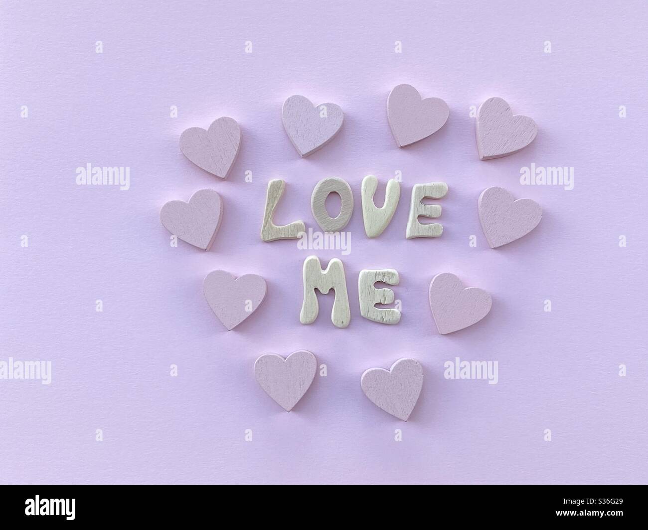 Message Love Me composé de lettres en bois faites à la main et coeur sur couleur rose - Image de stock capturée avec un smartphone