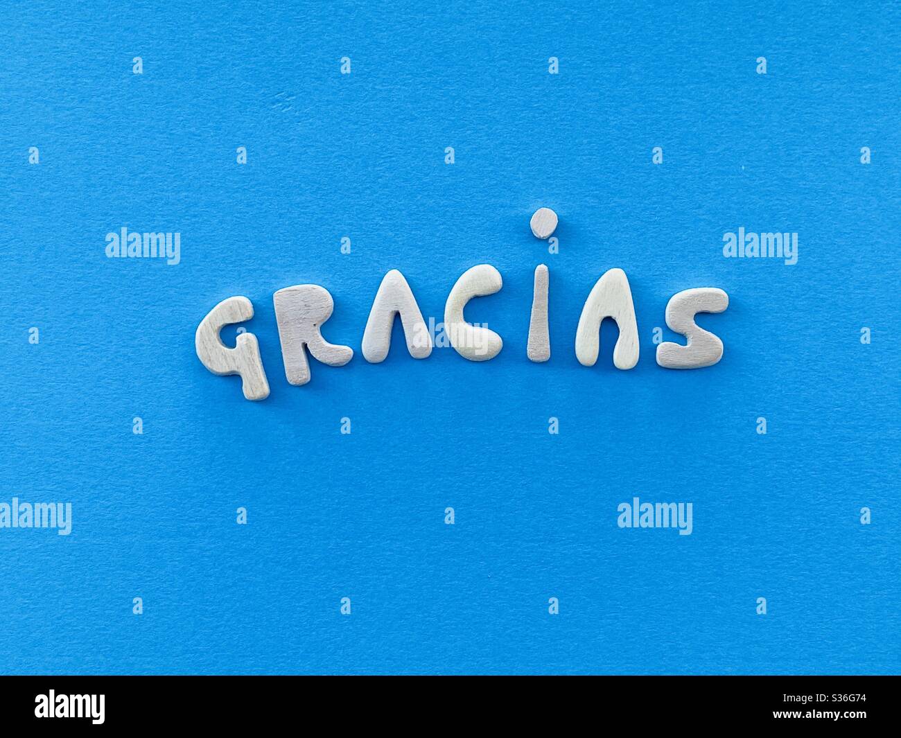 Gracias, merci en espagnol composé de lettres en bois faites à la main sur la couleur bleue - Image de stock capturée avec un smartphone