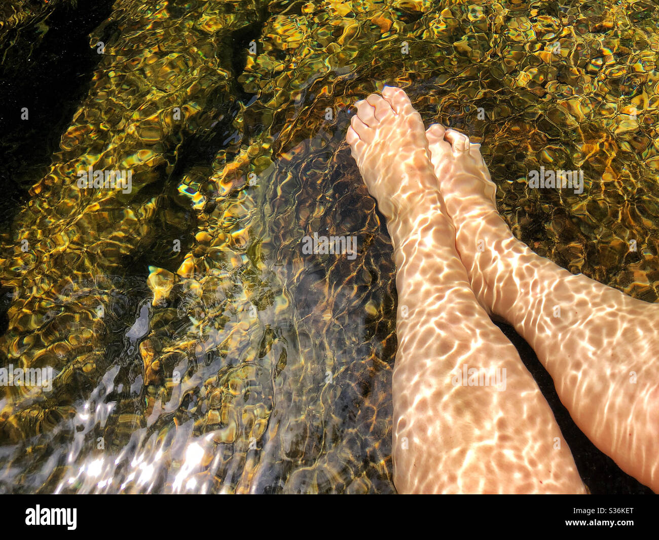 Femme se détendant au trou de baignade au lac sur la montagne, plongeant les pieds dans l'eau froide Banque D'Images